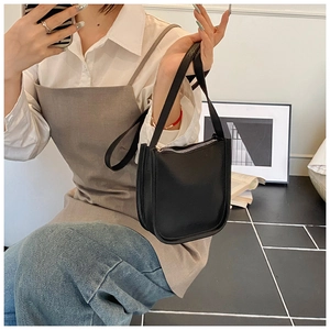 Detailed side view of a black lychee texture bucket bag worn by a model in a room