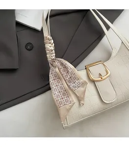 Détail du sac sous le bras crème avec texture crocodile et décoration en écharpe de soie
