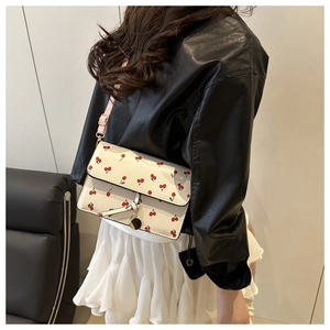 Close-up of white rectangular shoulder bag with red cherry pattern and pink striped strap
