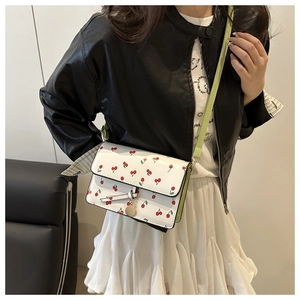 Detail view of white cherry print crossbody bag worn with black jacket and white skirt