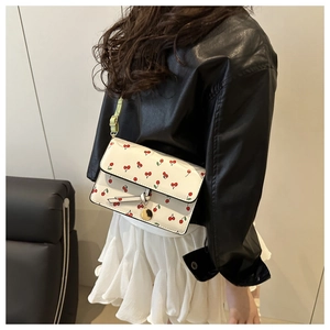 Detail of white cherry print crossbody bag featuring leather tie and gold pendant