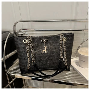 Detail of black woven tote bag with V-shaped texture, gold chain strap, and deer charm