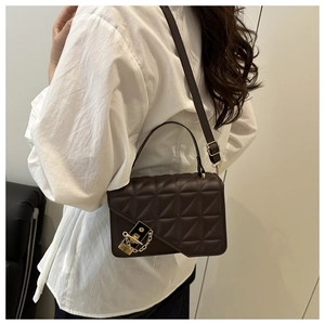 Detail of dark brown quilted shoulder bag with golden buckle and chain on white shirt