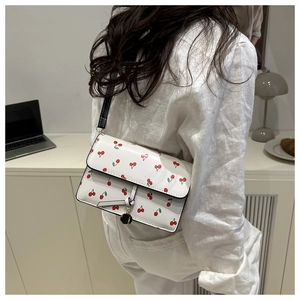 Close-up of white crossbody bag with red cherry patterns and metal pendant detail