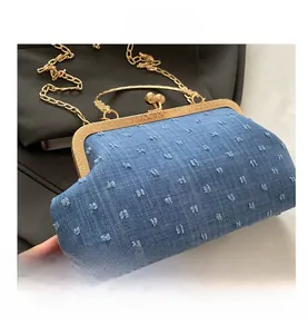 Close-up of blue denim crossbody bag with fuzzy pom-poms and gold metal frame kiss lock