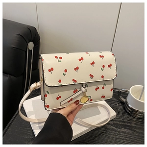 Close-up of white rectangular crossbody bag with cherry prints and gold metal pendant