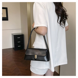 Detailed side view of a black glossy underarm bag with gold metal clasp on a white suit