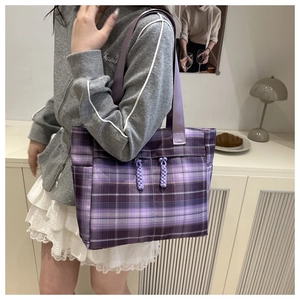 Detail of purple plaid tote bag with decorative drawstrings on model in soft home setting
