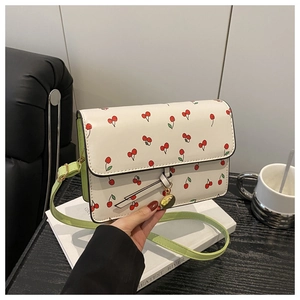 Detail of white leather cherry print crossbody bag with green strap and gold charm