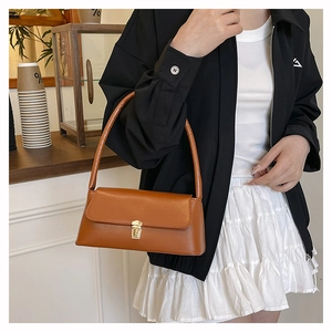 Detail of a brown leather shoulder bag with a gold rectangular metal swivel clasp