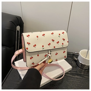 Detail of white cherry print crossbody bag with pink leather strap and gold pendant
