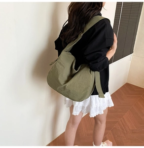 Large olive green nylon tote bag with wide strap shown in a minimalist interior setting