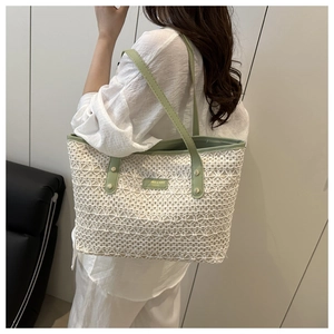 Detail of hollow-out straw woven tote bag with green leather straps and logo patch