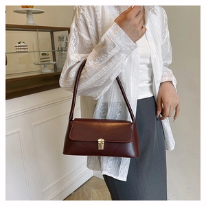 Close-up of elegant burgundy glossy leather underarm bag with gold metal buckle