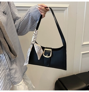 Detail of black croc-effect underarm bag featuring a gold buckle and decorative silk scarf