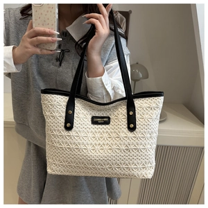 Detail of elegant beige lace tote bag with black leather handles and branded tag