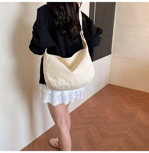 Detail shot of a large beige pleated fabric tote bag worn as a casual crossbody bag