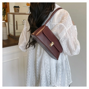 Model showing dark burgundy leather underarm bag with gold lock in cafe setting