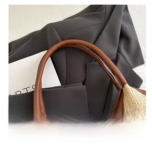 Detail of hand-woven straw bag featuring premium brown litchi grain leather handle