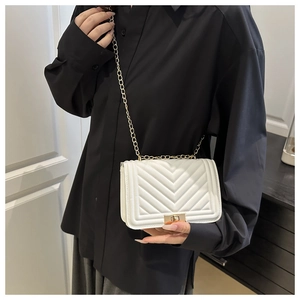 Detailed view of white quilted chain bag with gold rotating lock on black clothing