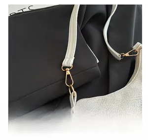 Detail of gold metal hook and white woven strap on a textured white shoulder bag