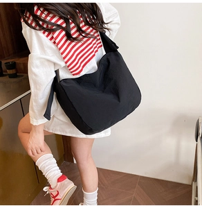 Dynamic view of a large black crossbody nylon tote bag worn by a model in casual style