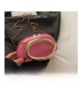 Detail view of pink patent shell bag featuring large gold C-handle and chain strap