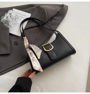 Detail of black croc-embossed baguette bag with gold buckle and silk scarf decoration