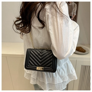 Detail of black quilted shoulder bag with V-shaped stitching and golden chain strap