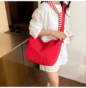Detail of red canvas crossbody bag with wide adjustable strap worn by model