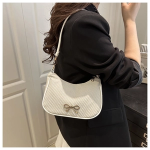 Detail of white woven underarm bag with gold bow clasp on a female model shoulder