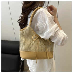 Detail of straw shoulder bag featuring a yellow bow tie and contrast leather base
