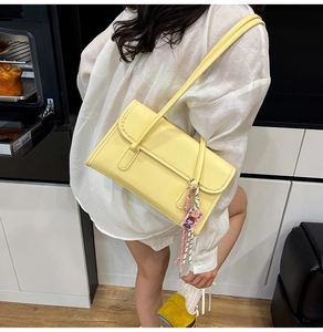 Detail of bright yellow underarm bag featuring contrast stitching and cute cartoon charm