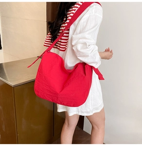 Detail view of large red hobo crossbody bag with wide shoulder strap worn by a model