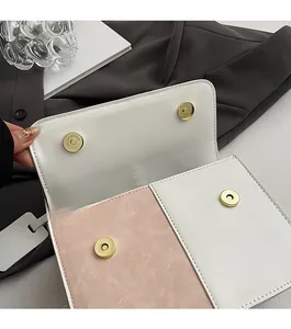 Detail view of dual gold magnetic buckles on white and pink leather crossbody bag