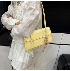 Detail view of a pale yellow PU leather shoulder bag with a cute pink cartoon pendant