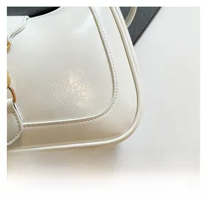 Close-up of glossy white faux leather baguette bag with crinkled texture and fine stitching