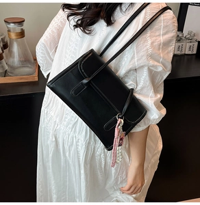 Detailed view of a black leather rectangular shoulder bag with a woven tassel charm