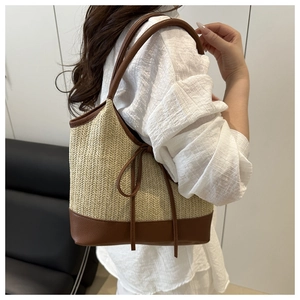 Close-up of woven straw tote bag with brown leather trim and decorative side bow detail