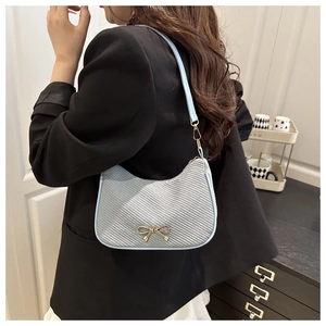 Detailed view of light blue shoulder bag featuring textured fabric and a gold bow buckle