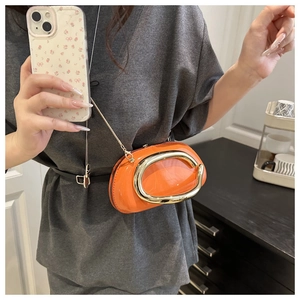 Detail of bright orange patent leather crossbody bag with bold gold metal C-ring buckle
