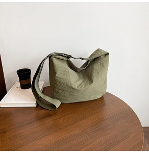 Detail of olive green large tote bag showing nylon texture and silver buckle on dark wood table
