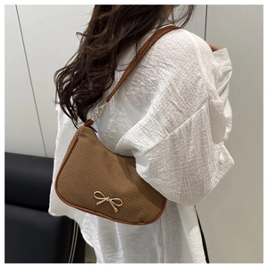 Detail of a brown ribbed knit underarm bag featuring a golden metal bow and leather trim