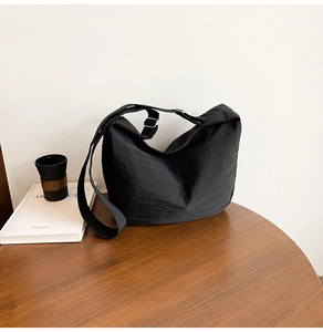 Detail of black large-capacity crossbody tote bag with soft texture on wooden table