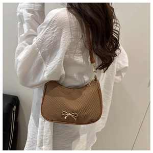Detail of solid color shoulder bag with herringbone texture and gold bow metal hardware