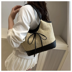 Detail of handwoven straw beach tote featuring black leather trim and decorative bow