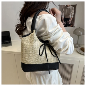 Detail of large woven straw tote bag with black leather bow and handle on a model