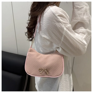 Pink shoulder bag with woven corduroy texture and a golden metal bow detail shown on a model