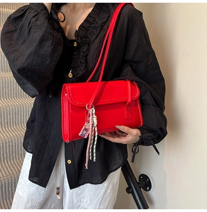 Detail of red PU leather shoulder bag with cartoon charm and woven pendant decoration