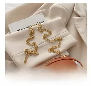 Detail view of a brown rugby-shaped crossbody bag with gold chain on a beige blazer